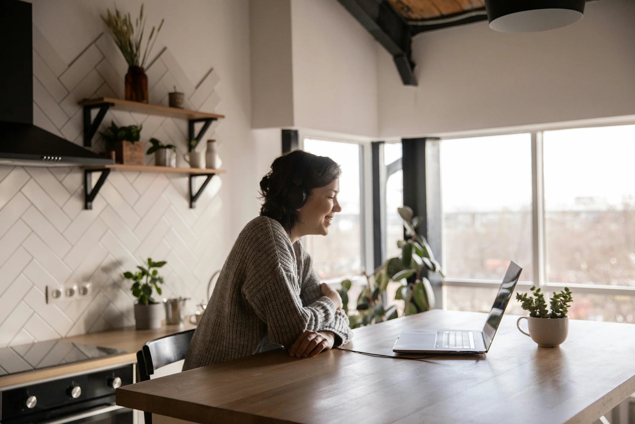 A woman with headphones speaking online from her kitchen